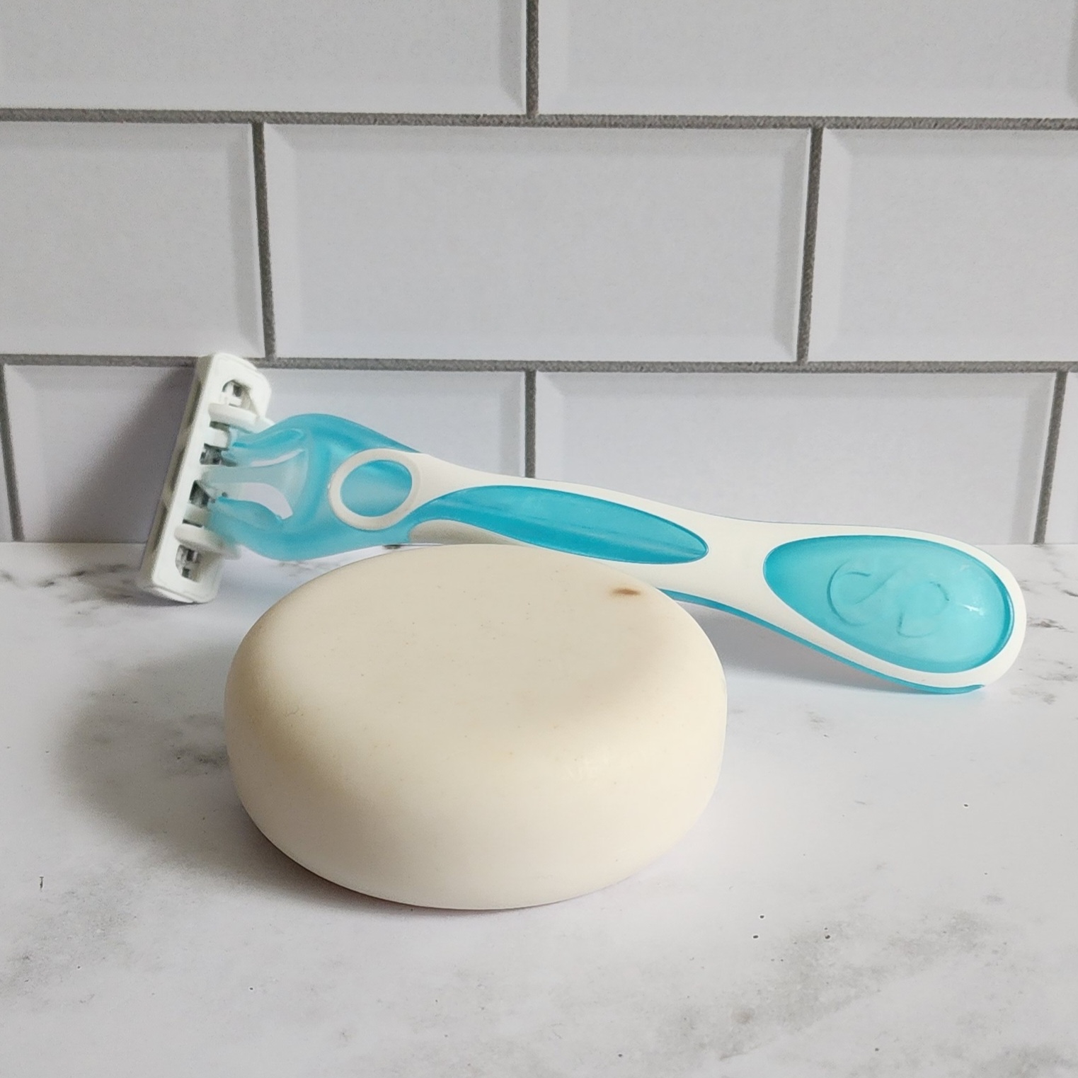 A cocoa butter and ashwagandha cleansing shave bar rests on top of a marble bathroom countertop.