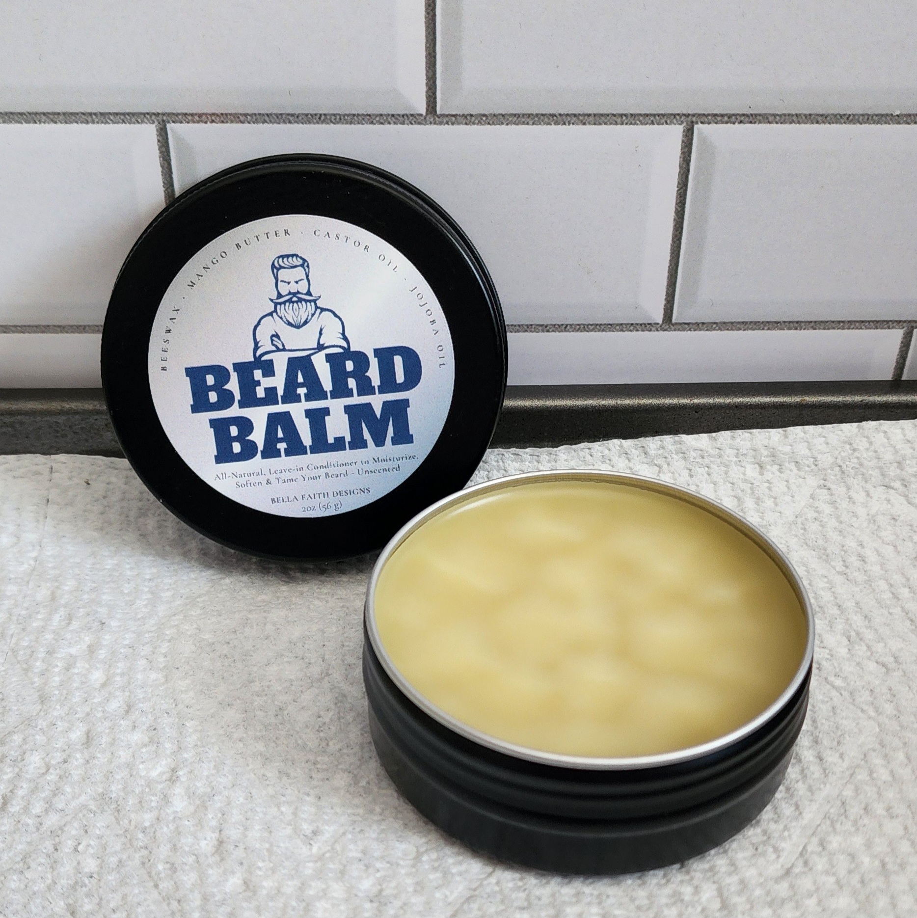 A 2oz black aluminum tin and a screw lid with a label that reads Beard Balm.