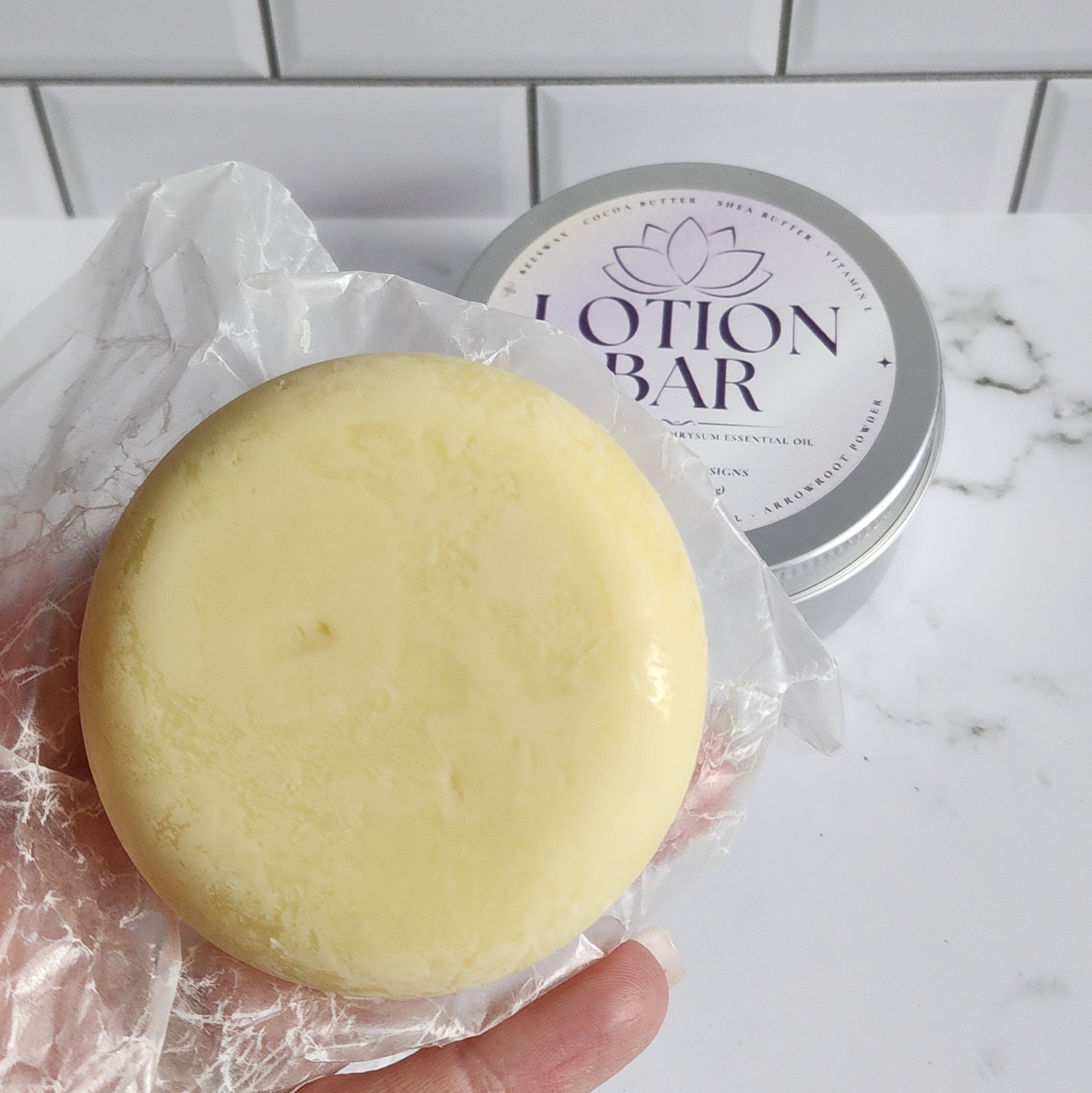 A solid lotion bar wrapped in a sheet of wax paper for storage in a tin jar with a screw on lid.