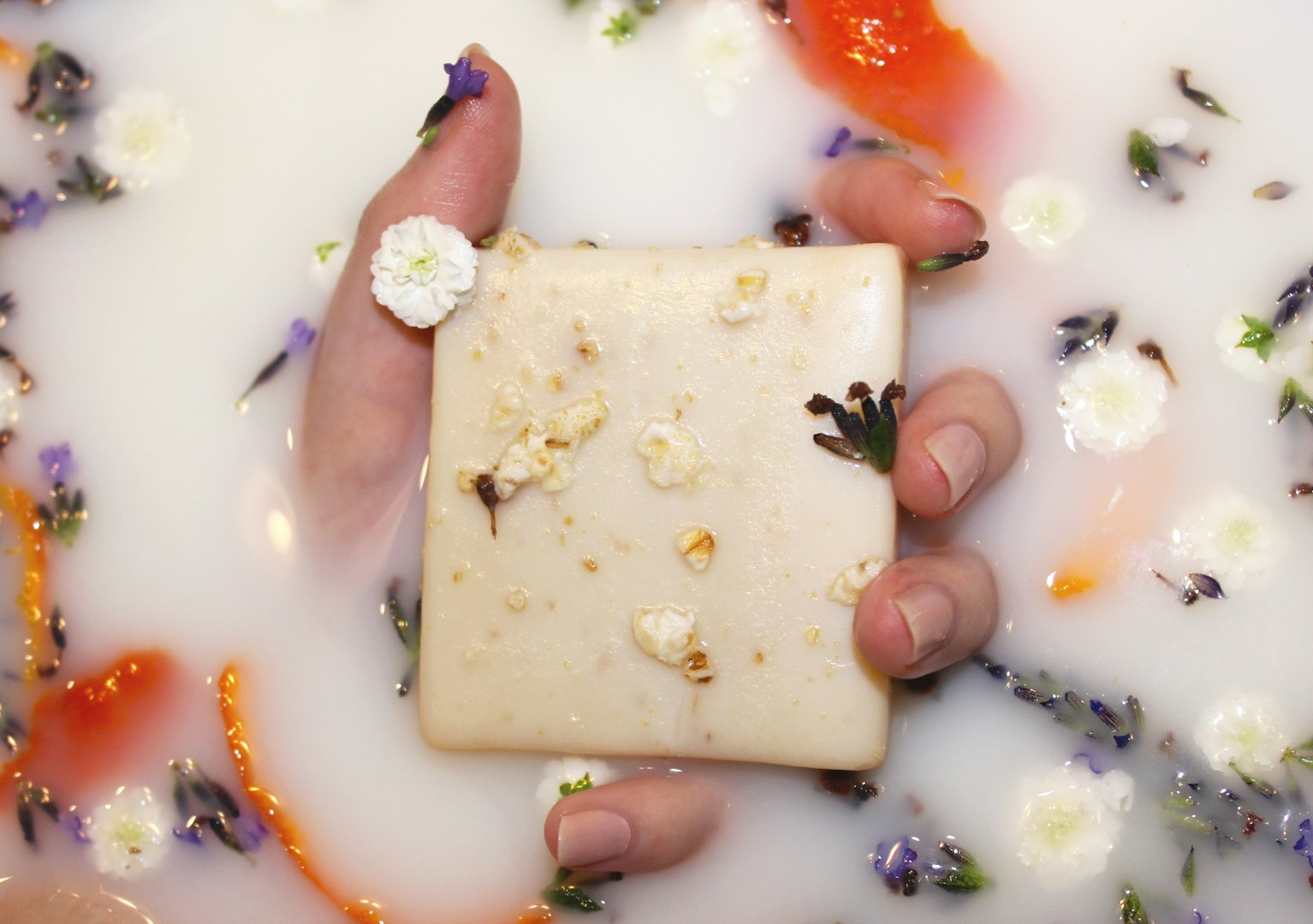 White square soap being used in a bath with flowers.